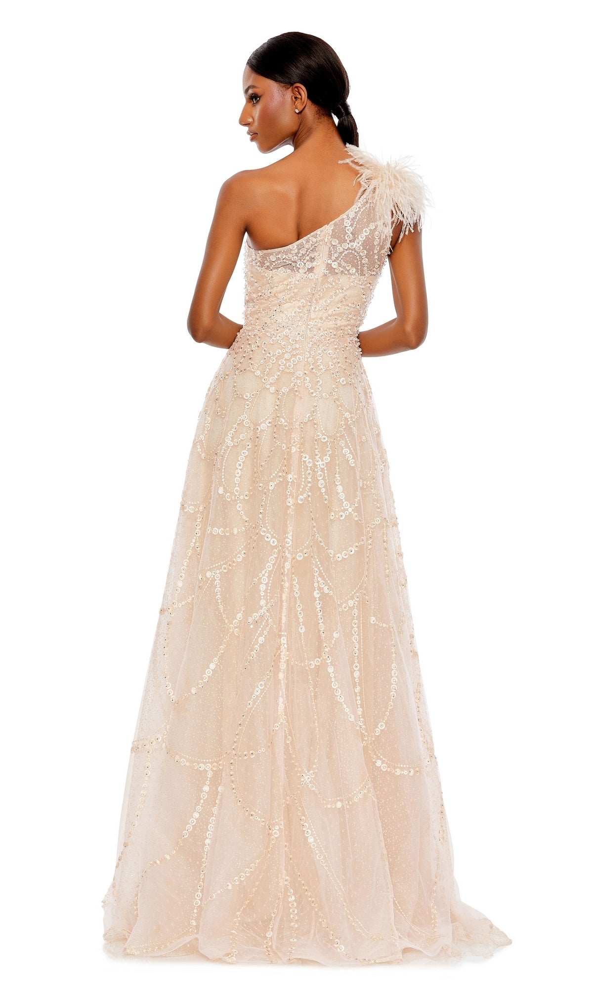 Woman in the Mac Duggal 20389 Beaded One-Shoulder Prom Gown, featuring a beige hue, sequin embellishments, and feather detail on the strap, stands with her back to the camera.
